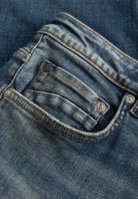 Κοντινή λήψη μπλε τζιν με μπροστινή τσέπη, μικρή τσέπη για κέρματα, ραφές και μεταλλικά πριτσίνια.