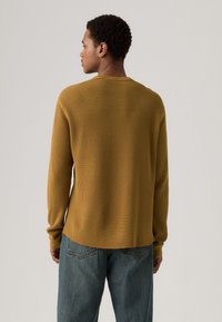 Langermet, sennepsgul ribbet strikkegenser med rund hals og en avslappet passform, kombinert med lyseblå jeans med rett ben.