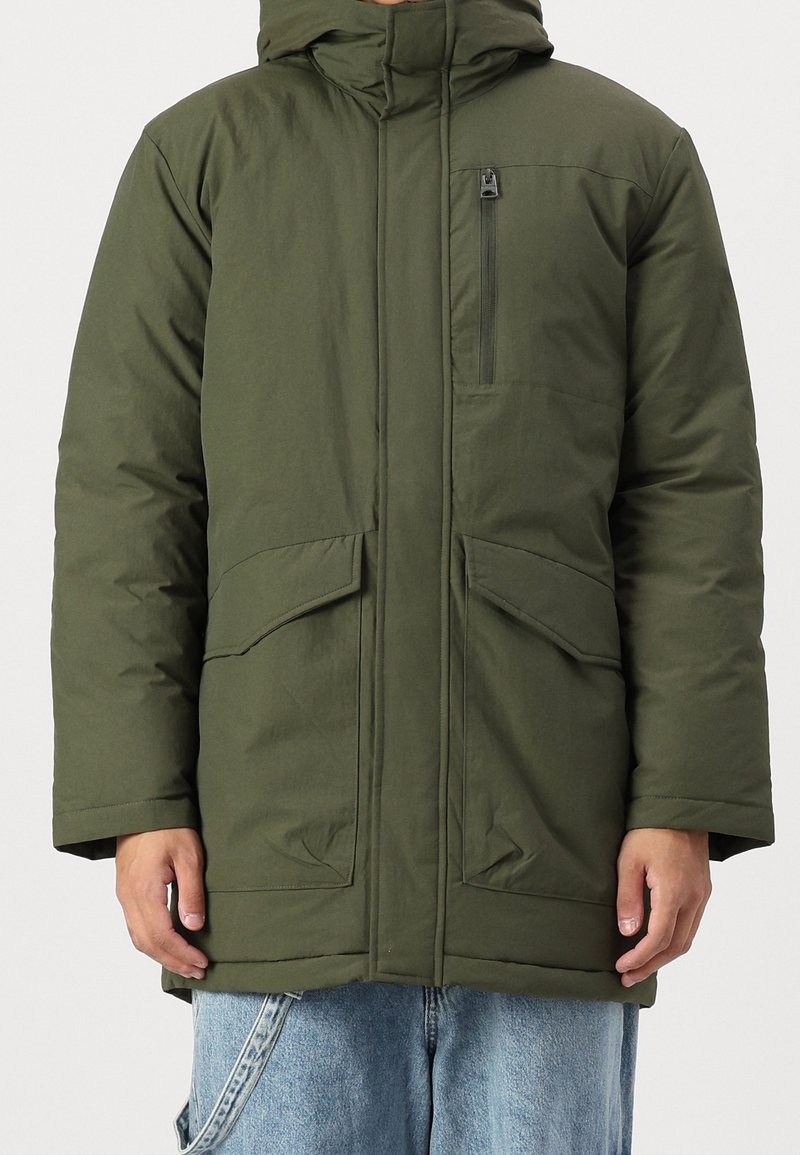 Chaqueta acolchada de color verde oliva con capucha, bolsillo en el pecho con cremallera y dos bolsillos delanteros; textura suave y diseño robusto.