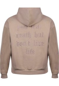 Sweat-shirt à capuche en coton beige clair avec finition texturée. Il présente un texte brodé au dos en beige foncé, des bords arrondis et des poignets côtelés.