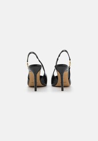 Črne slingback pete iz usnja z embosiranim vzorcem krokodila, s koničastim stiletto petami in zlate barve zaponko na zaponki okoli gležnja.