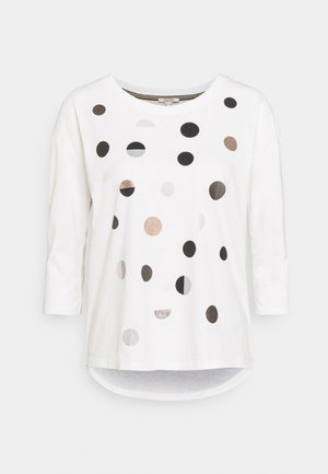 Chemise blanche à manches longues avec col rond, ornée de pois dispersés noirs, marron et gris de différentes tailles sur le devant.