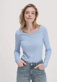 Lichtblauw langemouwen shirt van zacht materiaal met een ronde halslijn. Gecombineerd met hoge taille blauwe spijkerbroeken.