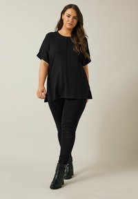 Sort løs top med korte ærmer, parret med sorte slim-fit jeans og sorte ankelstøvler. Glat tekstur og enkelt design.