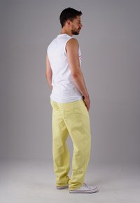 Sleeveless white shirt with red stripe, paired with loose yellow pants and white sneakers; showcased from the side.