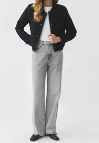 Černá bomber bunda s knoflíkovým zapínáním, nošená přes bílý tričko. V kombinaci s vysokými, světlými šedými volnými džíny a černými balerínami.