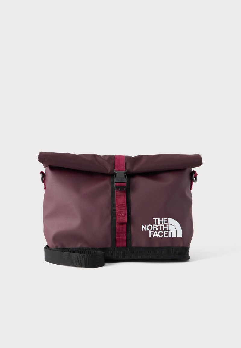 τσάντα ώμου North Face σε μπορντό με ρολό, μαύρο λουράκι, μπροστινή αγκράφα και λευκό λογότυπο σε μονόχρωμο φόντο.