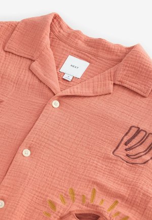Peach-colored short-sleeve shirt made of textured fabric, featuring buttons, a collar, and embroidered design with curved lines in yellow and brown.