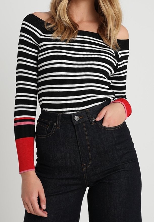 Zwart-wit gestreepte ribbel top met off-the-shoulder halslijn en rode accentmouwen. Gepaarde met hoog-getailleerde donkere spijkerbroeken.