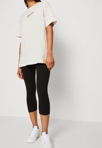 Beige bomulls t-shirt med en svart Nike-logotyp, i kombination med svarta leggings och vita sneakers, med en avslappnad passform och korta ärmar.