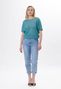 Top de punto turquesa con corte holgado, combinado con unos pantalones vaqueros de corte recto en azul claro. El conjunto presenta una silueta relajada y una textura suave.