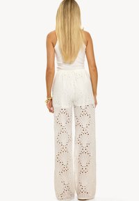 Witte, hooggewende broek van geborduurde stof met uitgesneden patronen, met een wijd uitlopende pijp en een gladde, aansluitende tailleband.