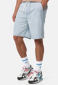 Shorts de mezclilla azul claro con cinturilla elástica y cordón. Bolsillos frontales y dobladillo cosido. Combinados con zapatillas predominantemente blancas.