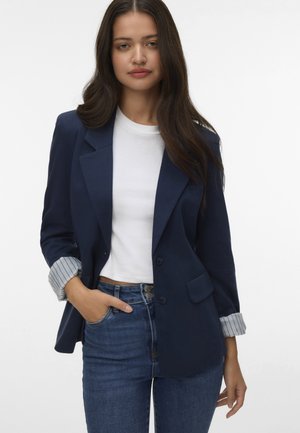 Marineblazer met een op maat gemaakte pasvorm, enkele knoopsluiting en gestreepte manchetten. Gecombineerd met een witte top en blauwe jeans.