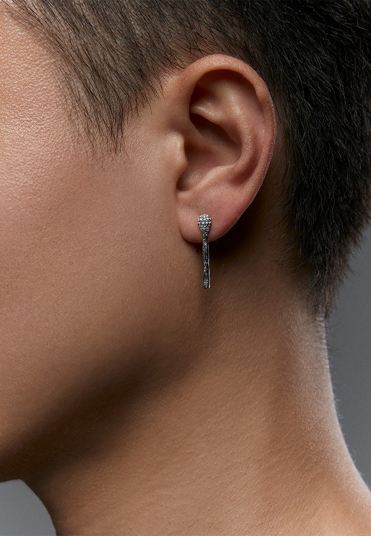 Cercei din argint cu un stud rotund decorat cu detalii strălucitoare și o lanț subțire, suspendat, cu textură, evidențiind un design modern.