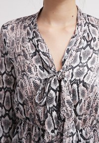 Blusa in stampa pitone rosa e nera con un nastro al collo, realizzata in un tessuto leggero e con una vestibilità comoda, ideale per un look informale.