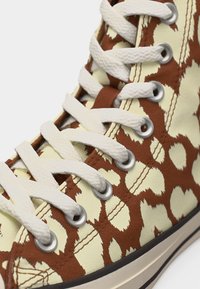 Αθλητικό παπούτσι με ψηλό αστράγαλο, εκρού και καφέ αφηρημένο μοτίβο, λευκά υφασμάτινα κορδόνια, ασημένια οπές και ραφές σε υλικό καμβά.