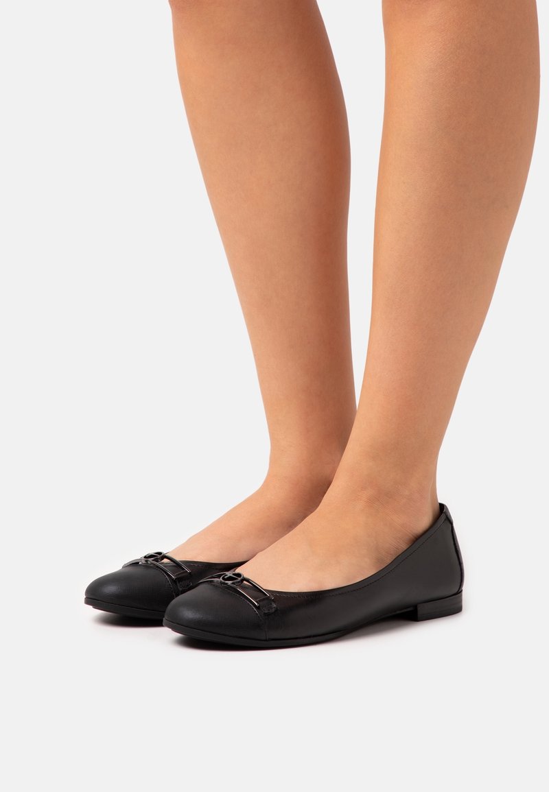 Black leather ballet flats with a rounded toe, decorative strap and buckle detail on the front, and a low, flat sole.