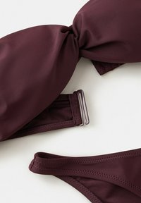 Ensemble bikini violet foncé avec haut torsadé et sangle latérale réglable sur le bas, posé à plat sur fond blanc.