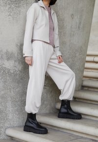 Lichtbeige cropped jack, lavendelkleurige trui, crèmekleurige wijde broek en zwarte enkellaarsjes met dikke zolen; gladde stof, minimalistisch ontwerp.