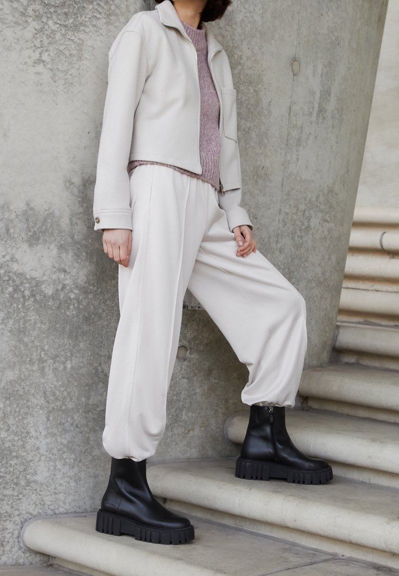 Lichtbeige cropped jack, lavendelkleurige trui, crèmekleurige wijde broek en zwarte enkellaarsjes met dikke zolen; gladde stof, minimalistisch ontwerp.