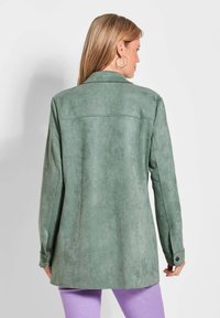 Groene suède jas met een kraag en lange mouwen, voorzien van knoopmanchetten en een gladde textuur. De achterkant toont een getailleerd ontwerp met naaddetails.