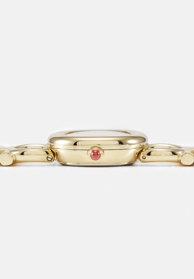 Gold-tone bracelet watch with a rounded case, featuring a red accent stone and a polished finish. The design includes a sleek, curved shape.