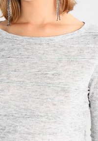 Jasnoszary sweter o miękkim, teksturowanym splocie. Szerokie dekolt i lekko dopasowany krój. Zawiera subtelne poziome paski.