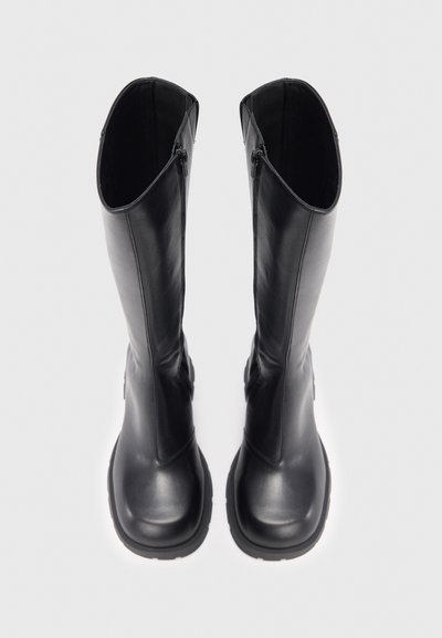 Botas pretas até ao joelho com acabamento em couro liso, biqueira arredondada e costura definida. Possuem fechos de correr laterais para fácil uso. Solas texturizadas.