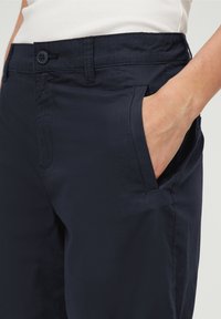 Pantalon bleu marine à la texture lisse, doté d'une fermeture à bouton, de poches latérales et de coutures cousues pour un look sur mesure.