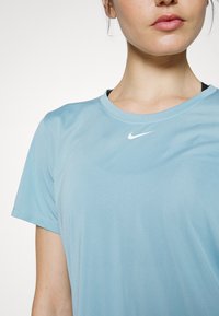 Světle modré sportovní tričko Nike s krátkými rukávy, kulatým výstřihem a bílým logem Nike na hrudi, vyrobené z hladké, na vlhkost odvádějící tkaniny.