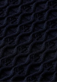 Granatowa tkanina o fakturze z wzorem diamentu z wypukłymi akcentami, wykonana z miękkiego dzianinowego materiału.