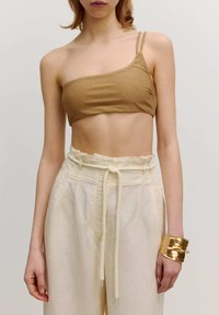 Bronzen metallic crop top met dunne bandjes, gecombineerd met lichtbeige, taps toelopende broeken en een gouden armband. Glede textuur, minimalistisch ontwerp.