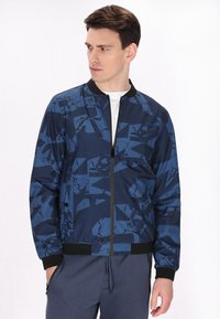 Blauwe bomberjack met een geometrisch patroon, gemaakt van lichtgewicht stof met een ritssluiting aan de voorkant, ribgebreide manchetten en tailleband.