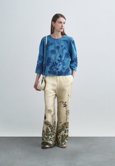 Μπλε τζιν τοπ με κεντήματα λουλουδιών, μανίκια 3/4, συνδυασμένο με ανοιχτό μπεζ σατέν παντελόνι με πολύχρωμα λουλουδάτα σχέδια. Μικρή λευκή τσάντα.