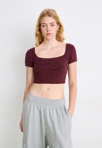 Top cropped de manga curta em marrom escuro, tecido texturizado com bainha canelada e logótipo preto discreto. Combinado com calças de moletom com elástico na cintura em cinza claro.
