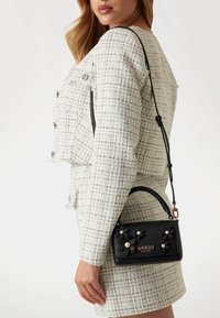 Black handbag with floral accents and pearl details, featuring a top handle and detachable shoulder strap. Textured design with logo.