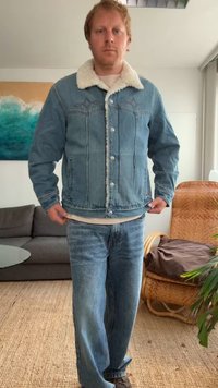 Veste en denim bleu clair avec un col en fausse fourrure blanche, boutons sur le devant et poches poitrine. Associée à un jean bleu clair.