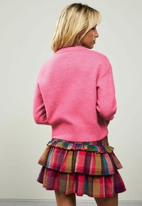 Suéter de punto rosa con dobladillo acanalado, combinado con una falda de cuadros en capas en vibrantes tonos de rosa, púrpura y amarillo. Tejido texturizado y volantes.