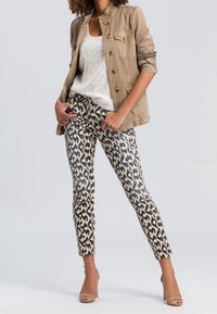 Veste militaire beige, top en sequins argentés et pantalon raccourci imprimé léopard avec une coupe slim. Des talons presque invisibles complètent le look.