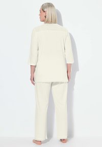 Conjunto de loungewear color crema que incluye una túnica larga con detalles de encaje en los hombros y el dobladillo, acompañada de pantalones rectos a juego.