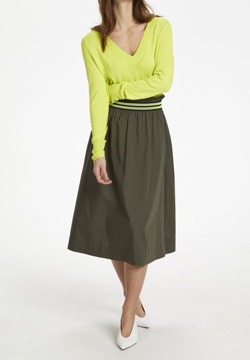 Suéter verde lima con escote en V y mangas largas, combinado con una falda verde oliva de longitud hasta la rodilla que presenta una cinturilla elástica y detalles de rayas negras.