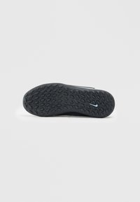Semelle de chaussure de sport noire avec un motif texturé, présentant des formes hexagonales et un petit accent logo bleu près du talon.