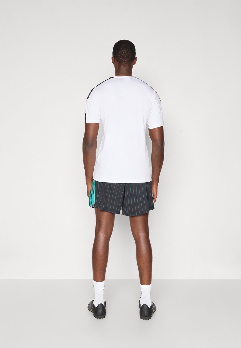 Chemise blanche à manches courtes avec des accents noirs aux épaules, assortie à un short noir avec des rayures teal et des rayures verticales.