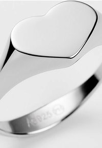 Silberring mit einer polierten herzförmigen Oberseite, glatten Kanten und einem runden Band mit eingravierten Markierungen auf der Innenseite.