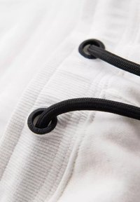 Gros plan d’un cordon noir passé à travers des œillets métalliques noirs sur un tissu côtelé blanc, montrant la texture et la couture détaillées.