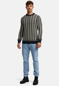 Pull en laine avec des rayures horizontales bleu marine et crème, col rond, bords-côtes aux manches et à l'ourlet, associé à un jean bleu clair et des bottes noires.