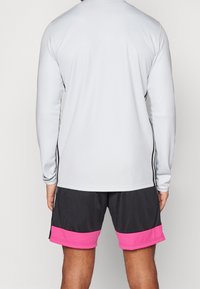 Långärmad ljusgrå träningsskjorta med svarta sidostråk, kombinerad med mörka shorts med en rosa kantdetalj. Slät tygtextur.