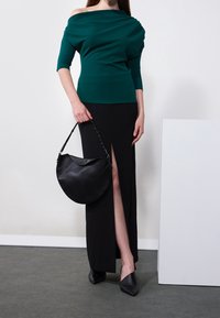 Teal off-shoulder topp, svart kjol med en sidoslits, bärandes en böjd svart handväska med kedjestropp, och spetsiga svarta klackar.