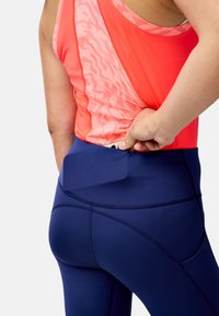 Débardeur de sport en corail avec un motif texturé, associé à un legging taille haute bleu marine avec une poche latérale et un tissu lisse.